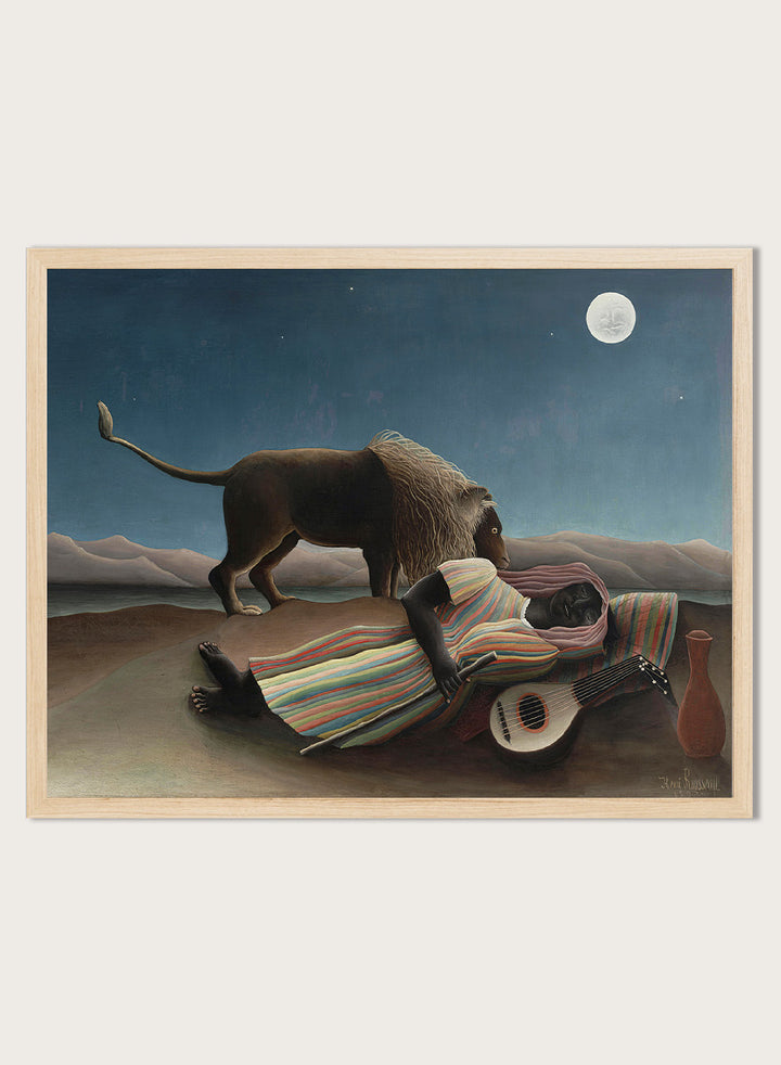A framed surreal art print depicting a lion standing over a sleeping person wrapped in a striped blanket, with a guitar, vase, and full moon in a night sky. The Sleeping Gypsy by Henri Rousseau is a vintage art print featuring a sleeping traveler, lion, moonlit desert, striped robe, mandolin, and deep blue night sky.