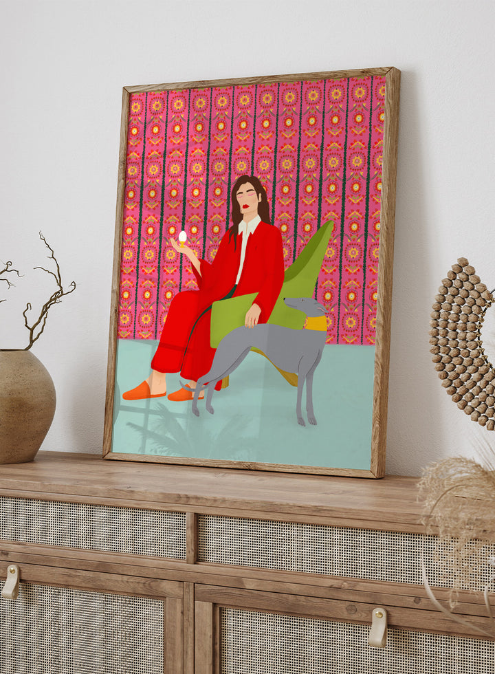Woman in a red coat sitting on a green chair with a dog, against a pink patterned wall. Wonderful Egg by Jota de Jai is a whimsical modern art print of a woman in a red robe holding an egg with her greyhound, officially licensed wall poster with framing.