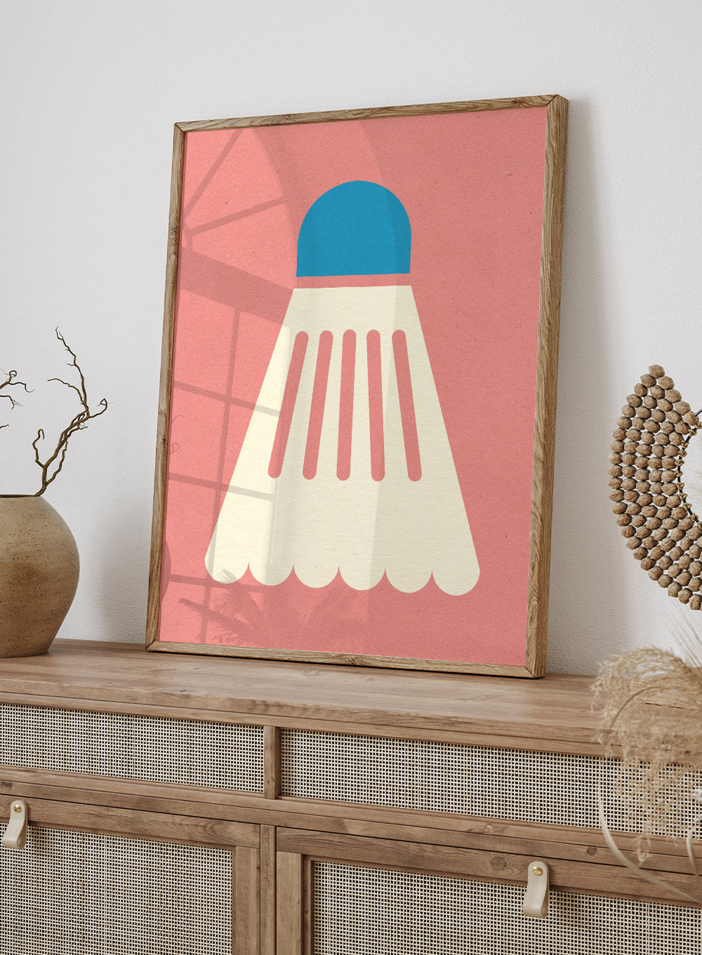 Shuttlecock with blue top and white body on a pink background. Badminton White Blue by Rosi Feist is a modern sports wall art print featuring a minimalist shuttlecock design in bold color and graphic poster style.