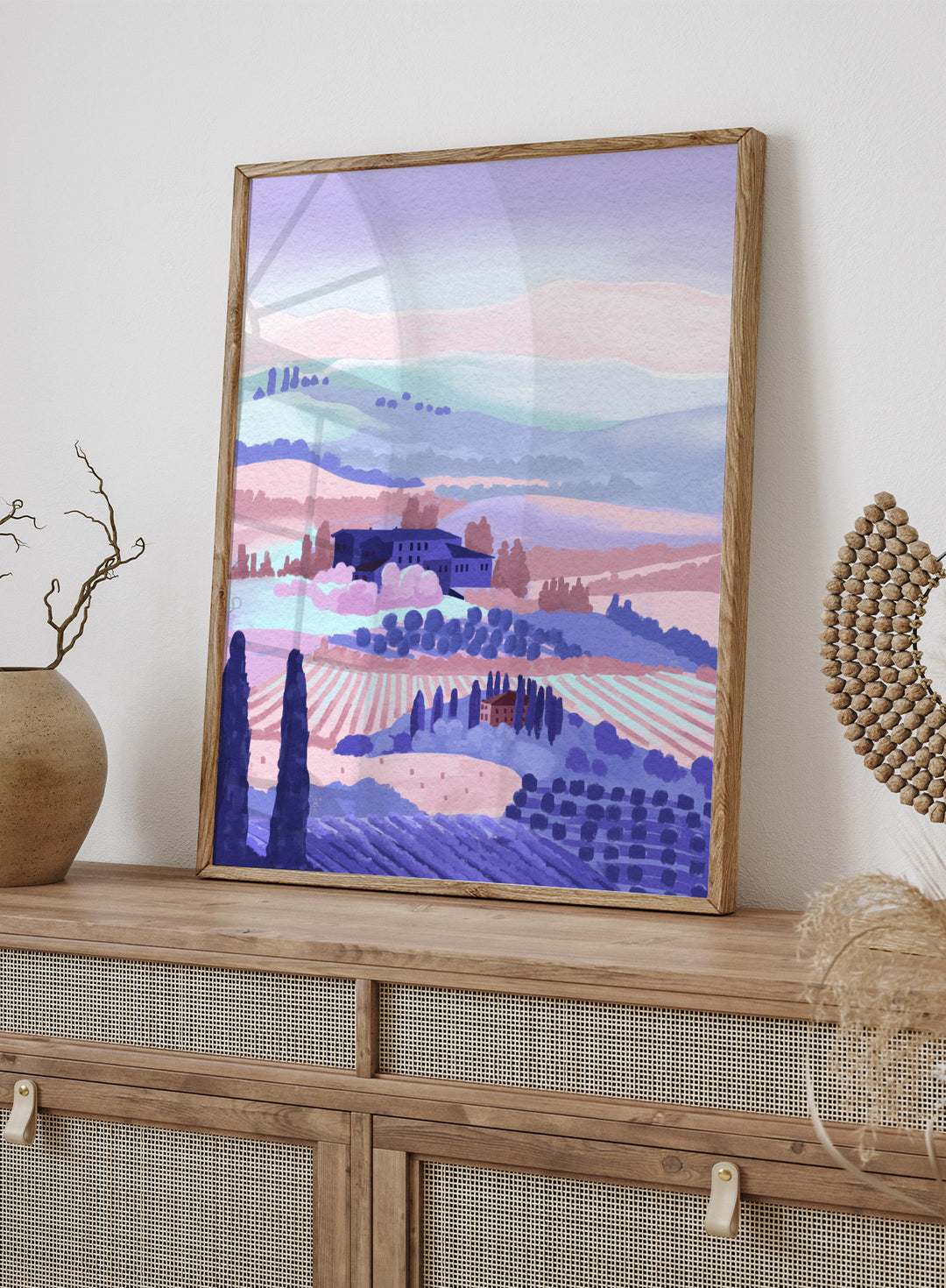Painting of a landscape with rolling hills, buildings, and cypress trees in pastel colors. Tuscany by Goed Blauw is a landscape art print and wall poster featuring rolling hills, fields, and countryside homes in soft pastel tones.