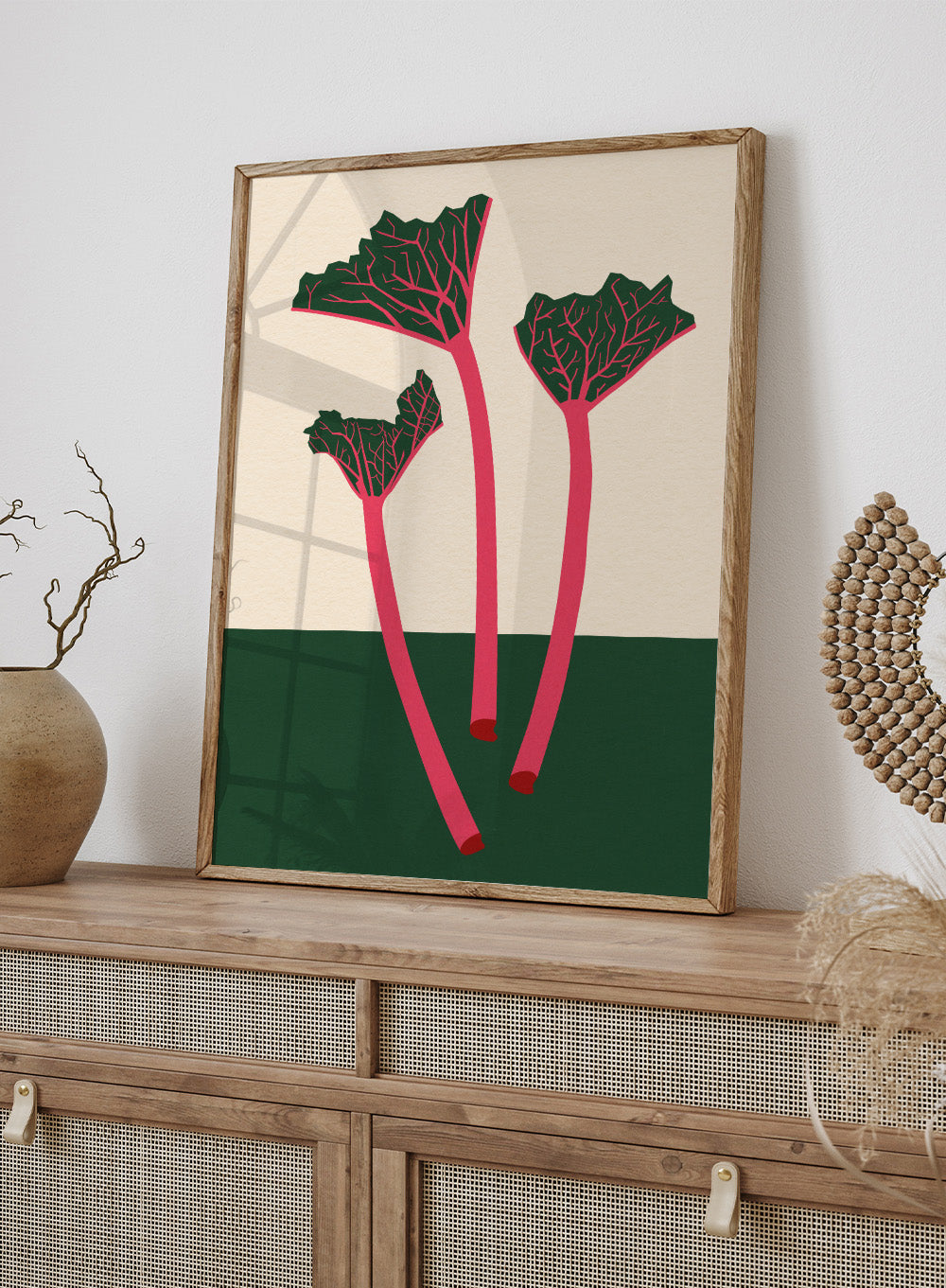 Illustration of red rhubarb stalks with green leaves on a beige and green background. Swedish Garden Rhubarb by Rosi Feist is a modern botanical art print with bold minimalist color and Bauhaus-inspired design. Officially licensed fine art poster with framing.