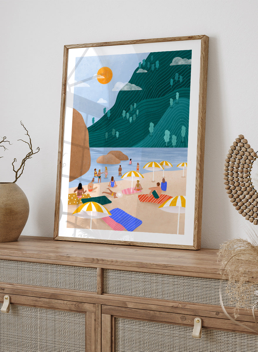 A framed art print featuring a stylized beach scene with a large teal-green mountain, blue water, a yellow sun, and beachgoers under striped umbrellas on a sandy shore. Relaxing Mountain Beach by Bea Müller coastal art print featuring swimmers, striped towels, yellow umbrellas, and a sweeping teal mountain.