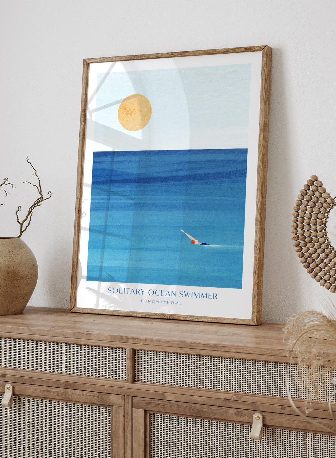 Art print of a solitary ocean swimmer with a large sun in the sky. Solitary Ocean Swimmer by Longwayhome is a minimalist ocean art print featuring deep blue water, lone swimmer imagery, and calming coastal wall art.