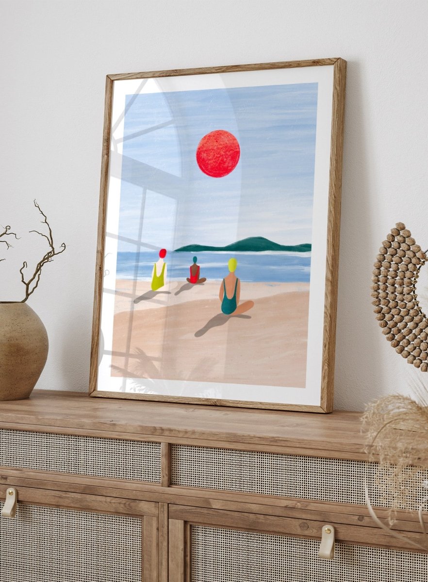 A minimalist art print depicting three figures meditating on a sandy beach under a large red sun. Red Sun Beach Serenity by Bea Müller premium fine art print featuring three figures on a beach beneath a bold red sun in a calm coastal setting.
