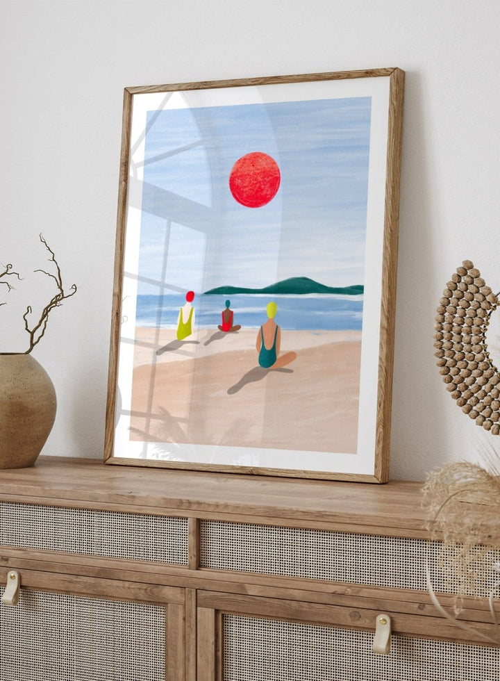 A minimalist art print depicting three figures meditating on a sandy beach under a large red sun. Red Sun Beach Serenity by Bea Müller premium fine art print featuring three figures on a beach beneath a bold red sun in a calm coastal setting.
