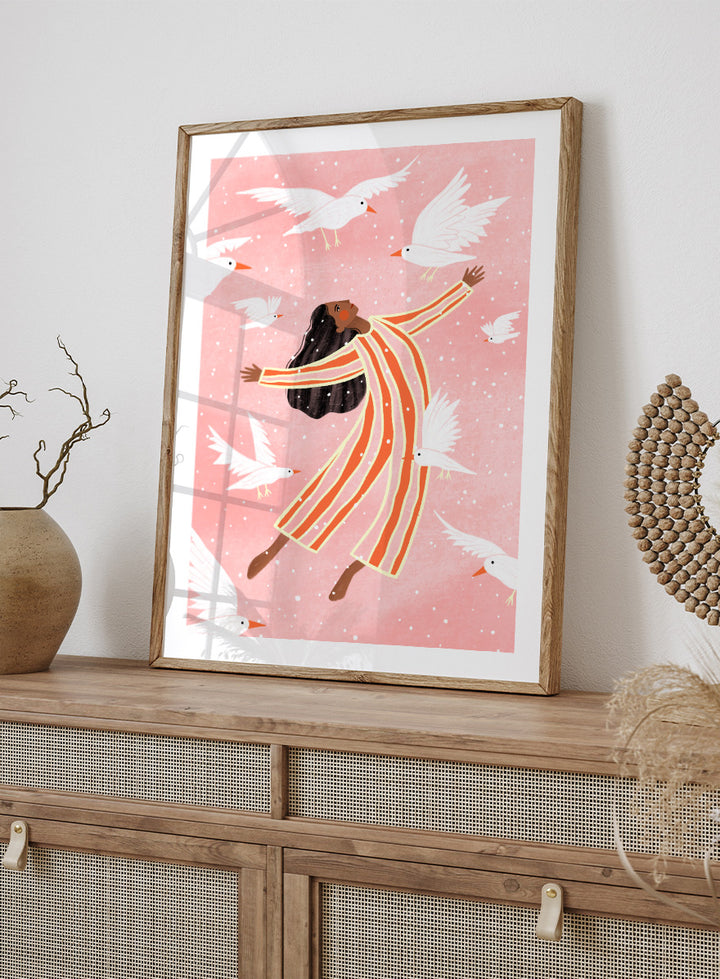 A framed art print featuring an illustration of a woman in orange and white striped pajamas floating among white doves on a soft pink background. Joyful Liberation by Bea Müller woman art print featuring a free-spirited figure surrounded by white birds in bold pink and orange tones.