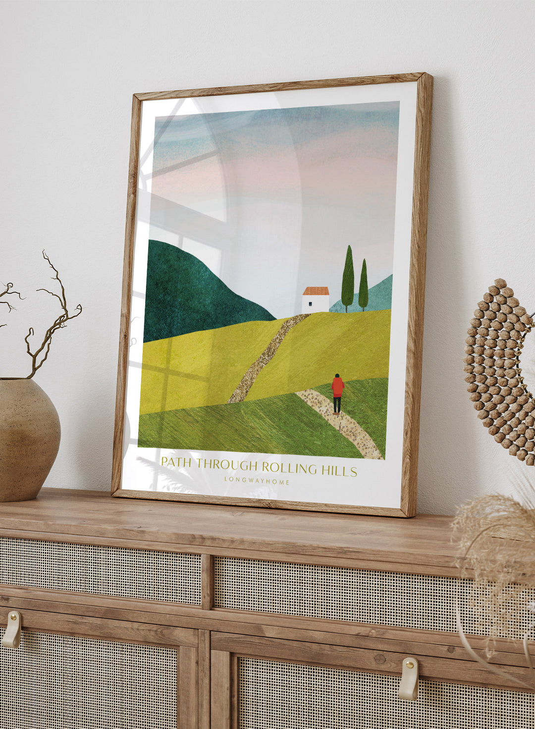 Illustration of a person walking along a path through rolling hills with a house and trees in the background. Path Through Rolling Hills by Longwayhome is a minimalist landscape art print featuring rolling green hills, countryside scenery, and modern travel inspired wall art.
