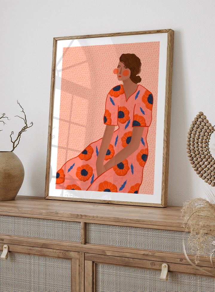 A stylized fashion illustration of a seated woman in a coral pink dress with large orange poppy motifs and blue leaf accents, shown with a white border and black frame. Stylish Poppy Portrait by Bea Müller floral woman art print featuring a pink dress covered in orange poppies and blue leaves for colorful modern wall decor.