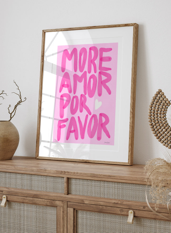 Pink text 'More Amor Por Favor' with a heart on a pink background. More Amor Por Favor by Baroo Bloom features bold pink hand-painted typography and a playful love message. Officially licensed wall poster with optional framing.