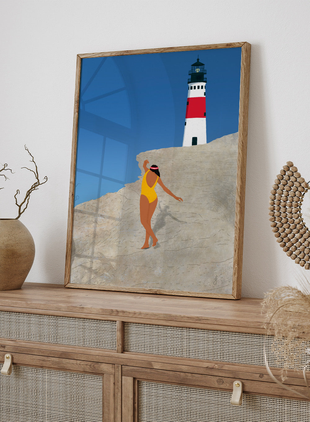 Woman in a yellow swimsuit standing on a rocky outcrop with a lighthouse in the background. My Beach by Jota de Jai is a modern coastal wall art print featuring a woman in a yellow swimsuit and a lighthouse. Officially licensed fine art poster with optional wood frame.