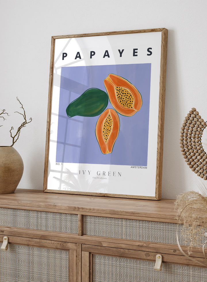 Illustration of papayas and a leaf on a blue background with 'Papayes' text at the top. Papayes by Ivy Green fruit art print featuring papaya illustration, modern food poster design, and colorful contemporary kitchen wall art.