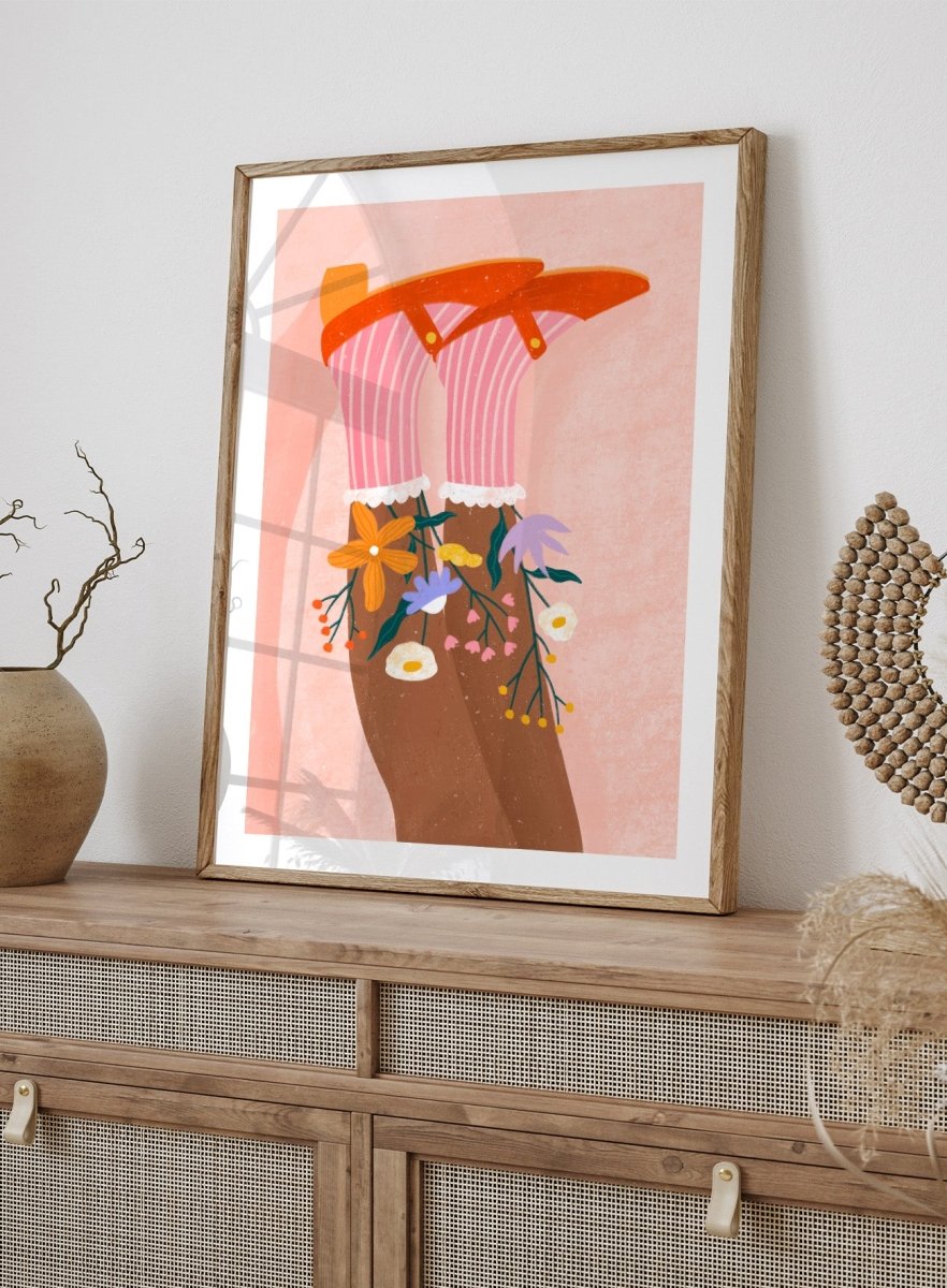 A stylized art print featuring a pair of legs wearing pink striped socks with white ruffles, decorated with colorful wildflowers, and topped with orange high-heeled shoes, set against a textured pink background. Happy Feet and Flowers by Bea Müller premium framed fine art print featuring red Mary Janes, striped socks, and colorful flowers on a soft pink background.