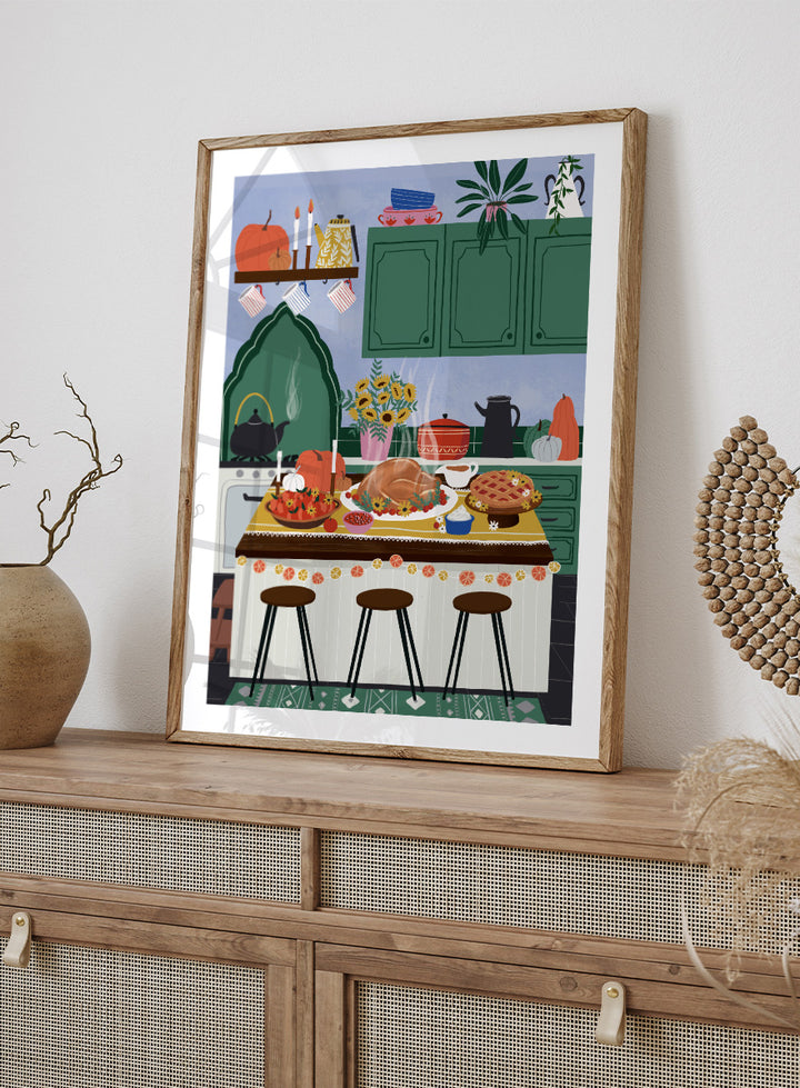 A framed art print depicting a cozy, stylized autumn kitchen scene with a large roasted turkey on a table covered in fall dishes, green cabinets, pumpkins, and three bar stools. Cozy Thanksgiving Kitchen by Ceyda Alasar kitchen art print featuring a turkey feast, pie, pumpkins, flowers, candles, and warm autumn decor.