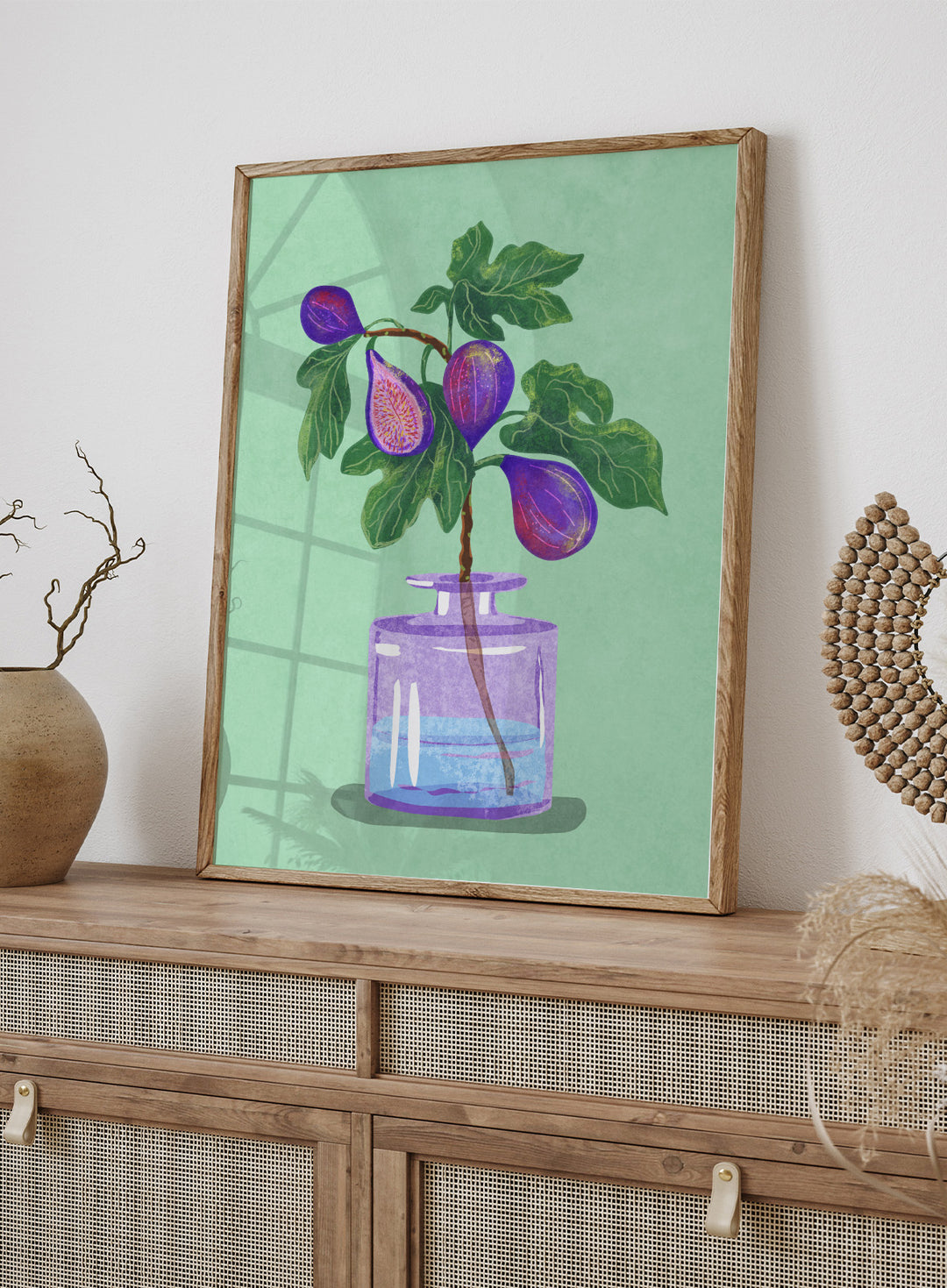 Illustration of a plant with purple fruits in a glass bottle on a green background. Figs Branch In Vase by Raissa Oltmanns is a modern fig still life art print with purple fruit and botanical kitchen wall poster design.