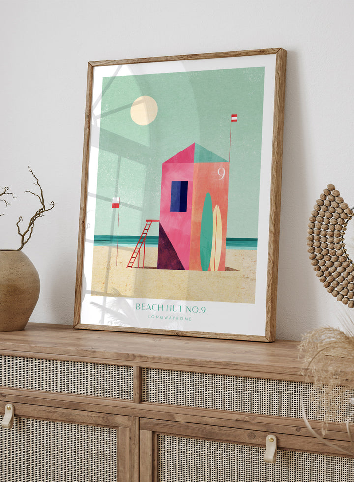 Colorful beach hut illustration with a minimalistic design on a light green background. Beach Hut Number Nine by Longwayhome is a retro inspired coastal art print featuring a colorful beach hut, surfboards, and minimalist seaside design.