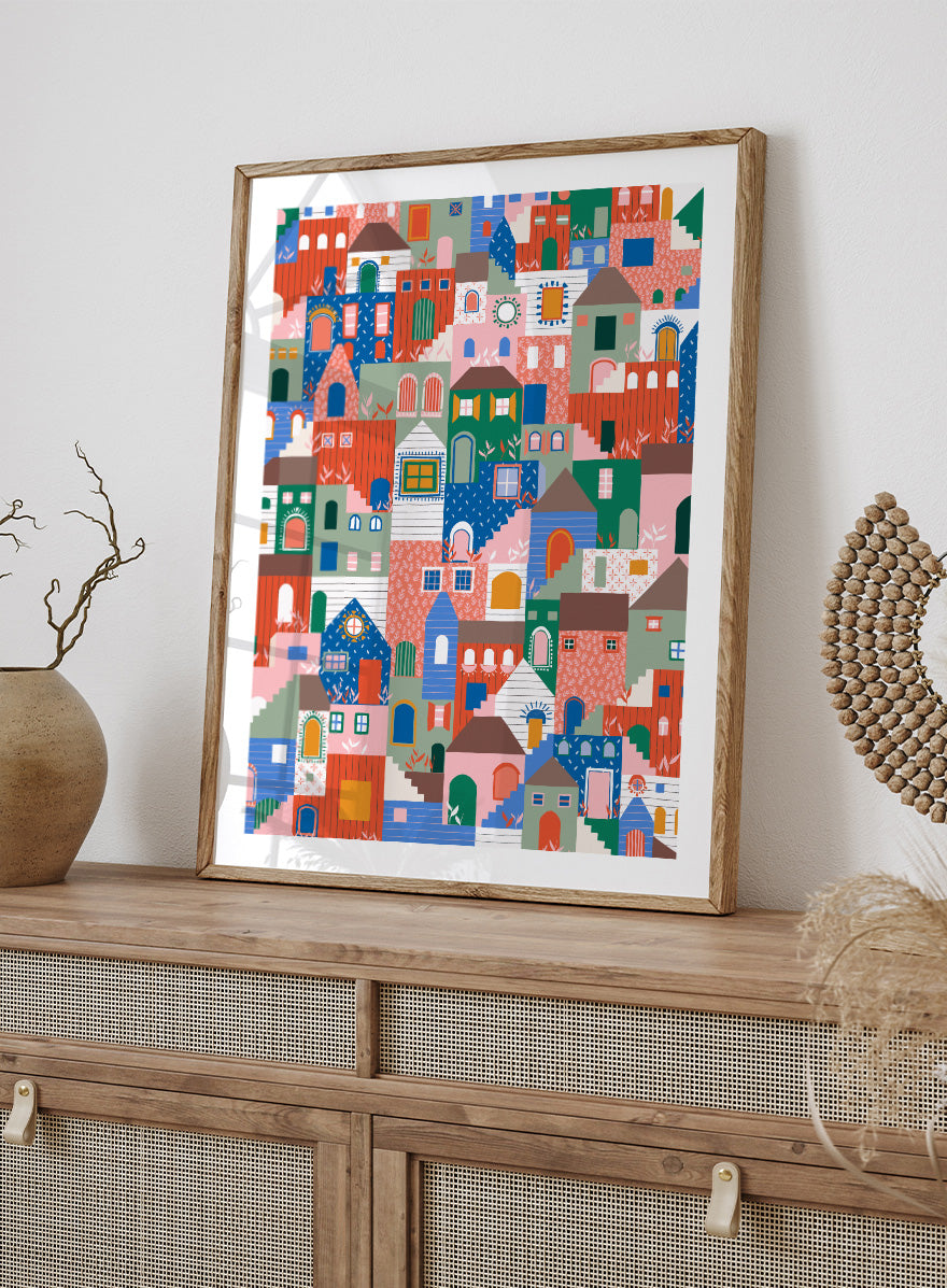A colorful art print featuring a dense, stylized illustration of houses and buildings in a playful, patterned village scene. Whimsical Cityscape Charm by Ceyda Alasar city art print featuring stacked colorful houses, patterned walls, winding stairs, and playful architectural details.