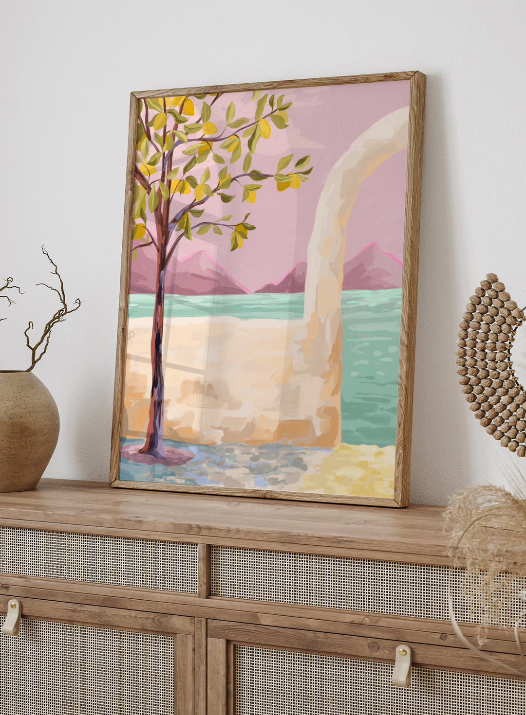 Artistic depiction of a tree by a lake with mountains in the background. Lemon Tree by Goed Blauw is a coastal art print and wall poster featuring a lemon tree, soft pastel sky, and ocean view in warm tones.
