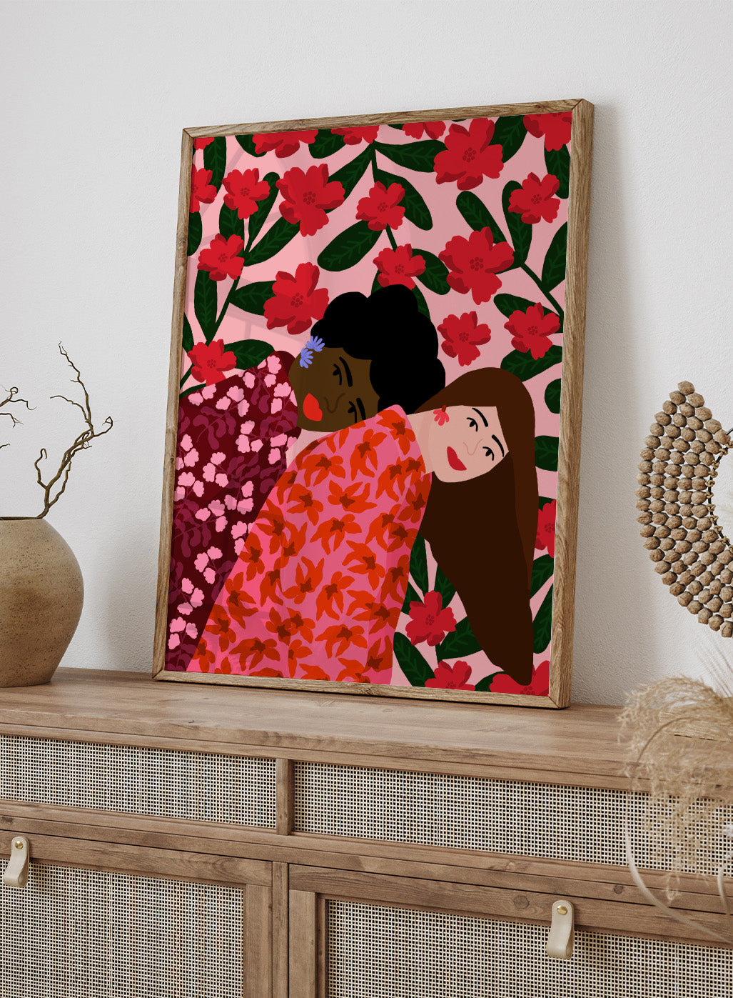 Illustration of two women embracing with a floral pattern in the background. Friendship by Rafaela Mascaro fine art print poster featuring two women embracing, red floral background, modern botanical wall art.