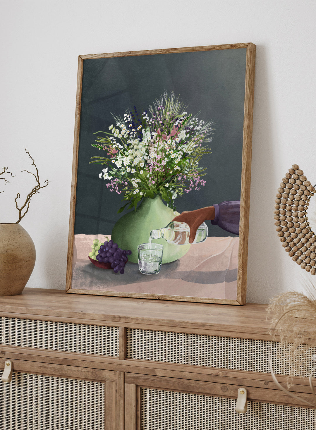 Still life with a green vase of flowers, grapes, and a glass being filled with a bottle. Frivolous Afternoon by Goed Blauw is a modern still life art print and wall poster featuring wildflowers, grapes, and a quiet pouring moment in soft, muted tones.
