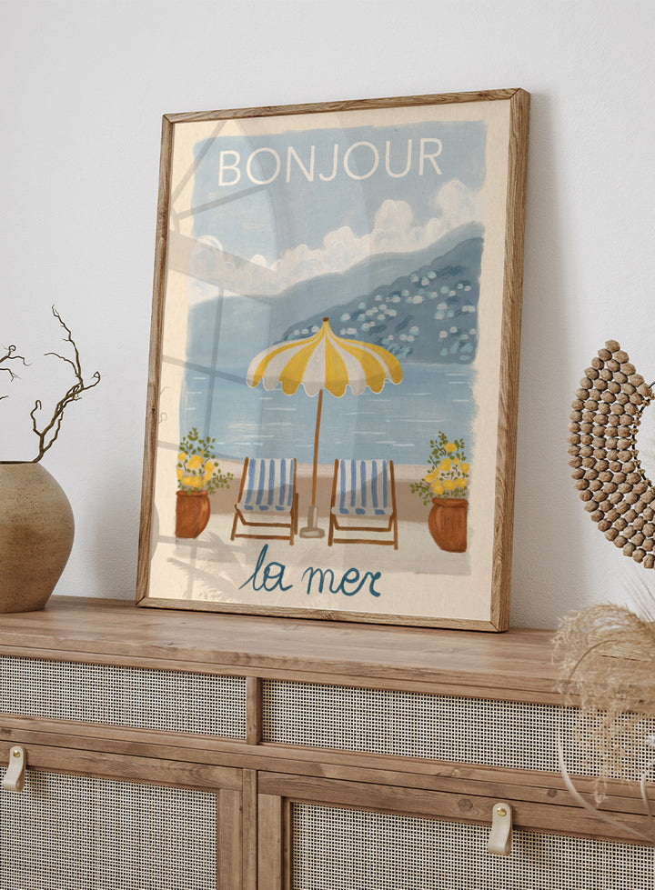 A vintage-style illustrated poster or print showing a beach scene with two striped lounge chairs under a yellow-and-white umbrella, potted plants, blue water, and mountains in the background. The words &
