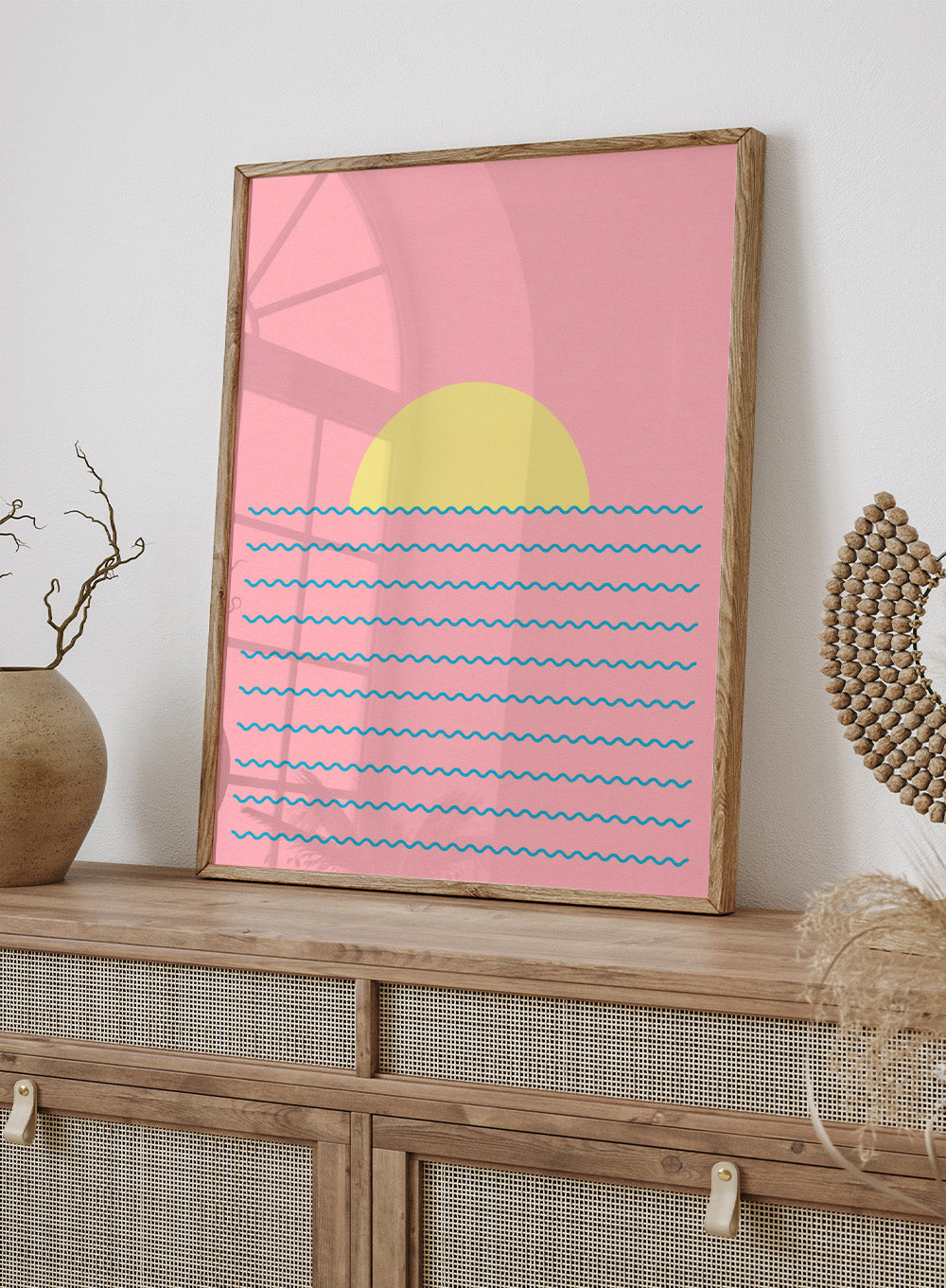 Simplified illustration of a sunset over water with blue waves on a pink background. Every Day the Sun Rises by Rosi Feist is a minimalist sun and waves art print with pink sky. Officially licensed modern poster with framing.