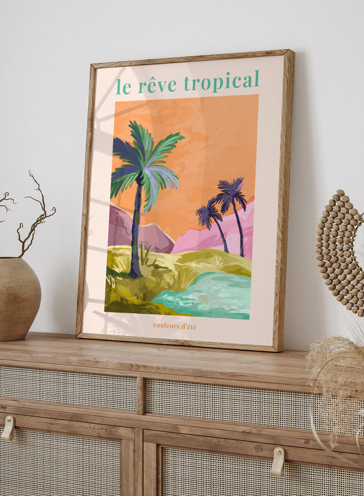Tropical landscape with palm trees and a lake, featuring the text 'le rève tropical' on an orange background. Le Rêve Tropical Palm Trees by Goed Blauw is a tropical landscape art print and wall poster featuring palm trees, hills, and water in warm sunset tones.