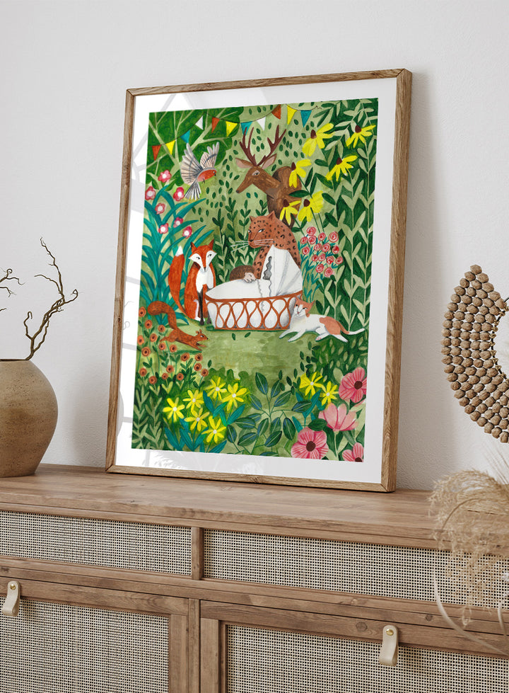 A framed art print featuring a whimsical forest illustration with animals gathered around a basket, surrounded by flowers and foliage. The print is shown with a white mat and a black frame against a white background. Welcome to the Forest by Caroline Bonne Müller woodland animal art print featuring a baby surrounded by a leopard, fox, deer, cat, flowers, and forest life.