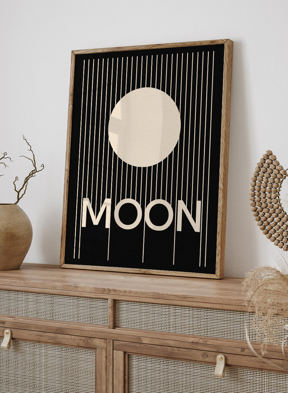 Poster with a stylized moon and the word 'MOON' on a black background. Moon by Rosi Feist is a bold minimalist Bauhaus-inspired art print with a cream circle and graphic lines. Officially licensed modern poster with framing.