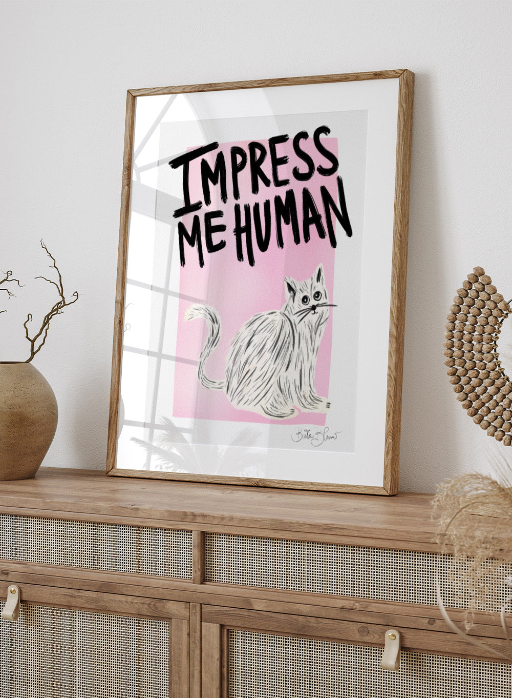 Cartoon cat with 'Impress Me Human' text on a pink background. Cat Owner. Impress Me Human by Baroo Bloom is a playful cat art print featuring hand-drawn illustration and humorous typography. Officially licensed wall poster with optional framing.