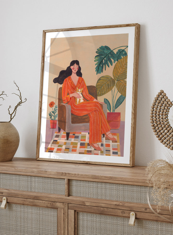 Illustration of a woman in an orange outfit sitting in a chair with plants around her. Cozy Home with Cat by Caroline Bonne Müller is a fine art print and wall poster featuring a woman in an orange outfit sitting with a cat in a warm, plant-filled interior.
