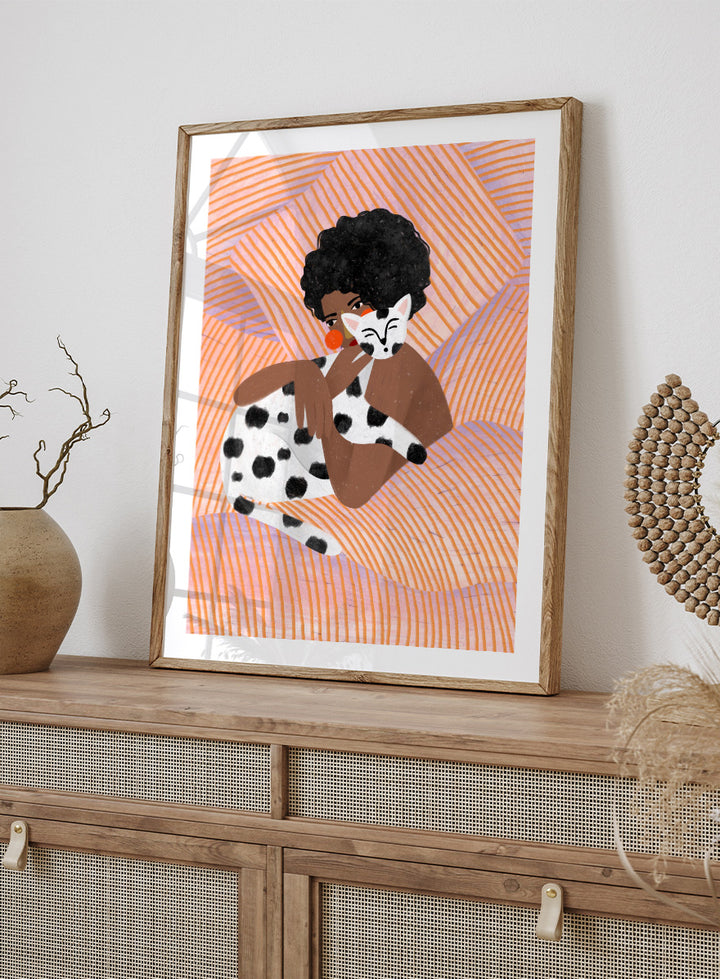 A framed art print featuring a stylized illustration of a person with an afro holding a black-and-white spotted cat, set against a peach and orange striped background. Cozy Cat Cuddles by Bea Müller animal art print featuring a woman embracing a spotted cat among soft peach and lilac stripes for cozy pet lover decor.