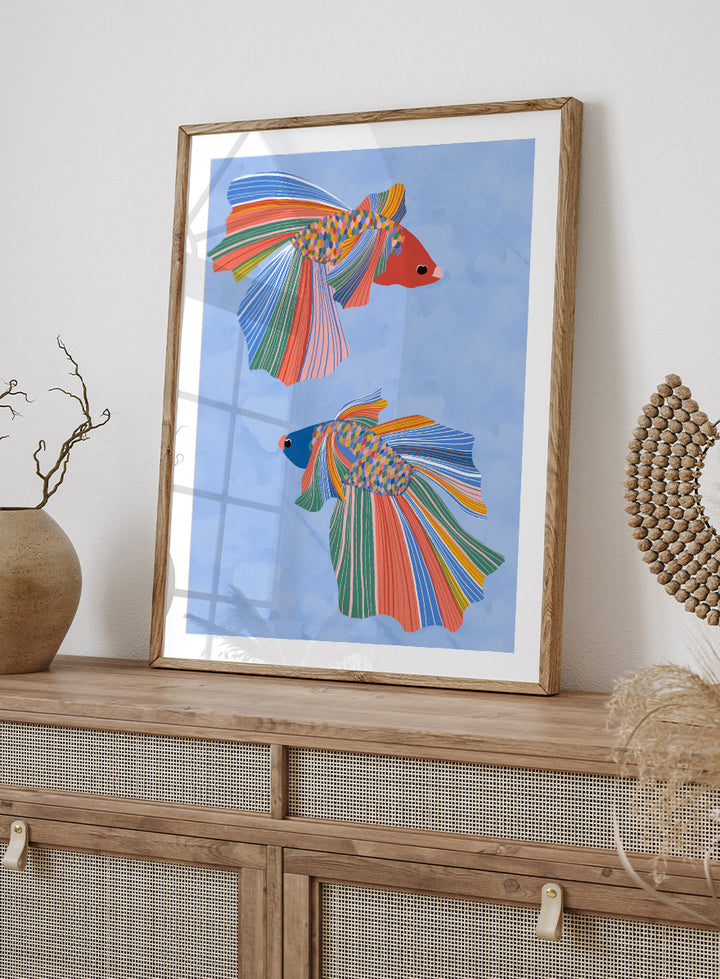 A framed art print featuring two stylized betta fish with vibrant, multicolored striped fins and bodies on a light blue water-like background. Colorful Betta Duo by Ceyda Alasar fish art print featuring two patterned betta fish with flowing fins in bright coral, blue, green, pink, and yellow.
