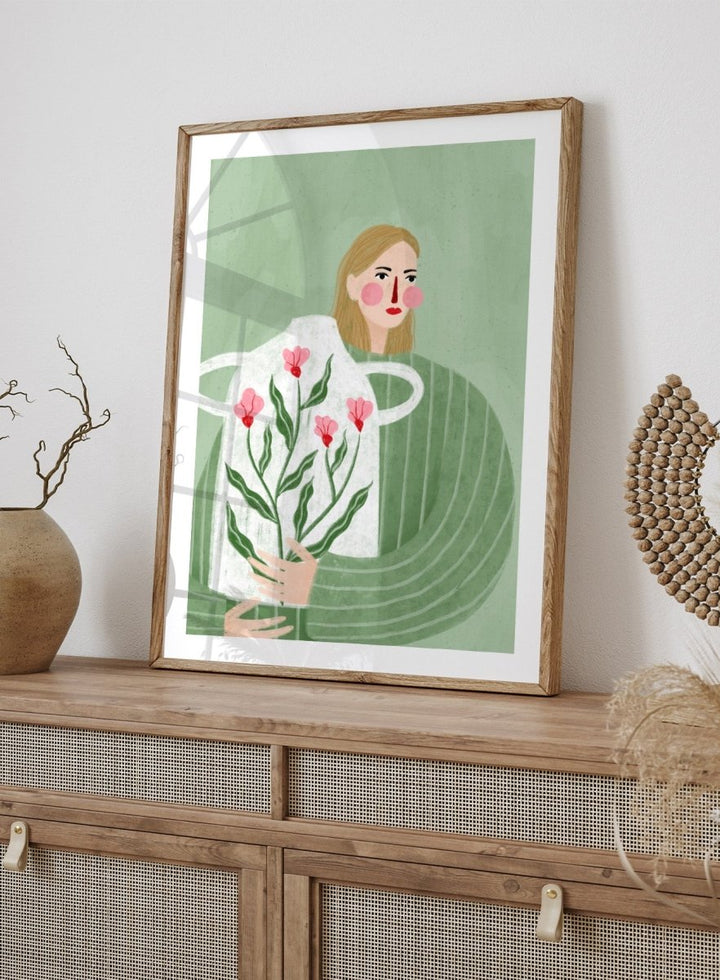 A framed art print featuring a stylized illustration of a woman with blonde hair holding a white apron decorated with pink flowers and green leaves, set against a sage green background. Woman Holding Flowers by Bea Müller premium framed fine art print featuring a woman carrying a white vase filled with pink flowers and green leaves.