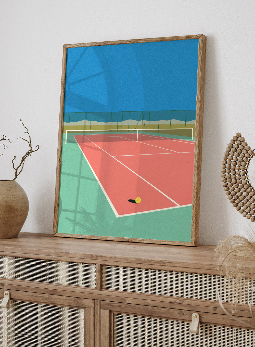 Illustration of a tennis court with a ball on the ground and mountains in the background. Tennis Court in the Desert by Rosi Feist is a modern minimalist fine art print of a pink tennis court in a surreal desert landscape. Officially licensed wall poster with optional artisan framing.