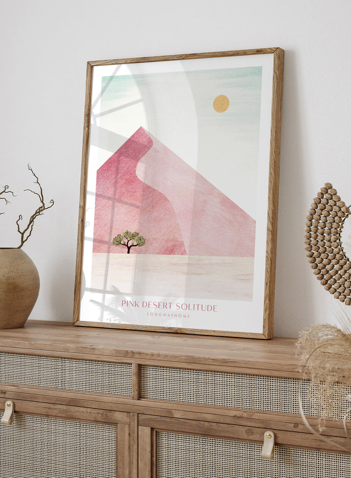 Artistic depiction of a pink desert with a solitary tree and a yellow sun. Pink Desert Solitude by Longwayhome is a minimalist desert art print featuring soft pink dunes, abstract landscape scenery, and calming modern design.