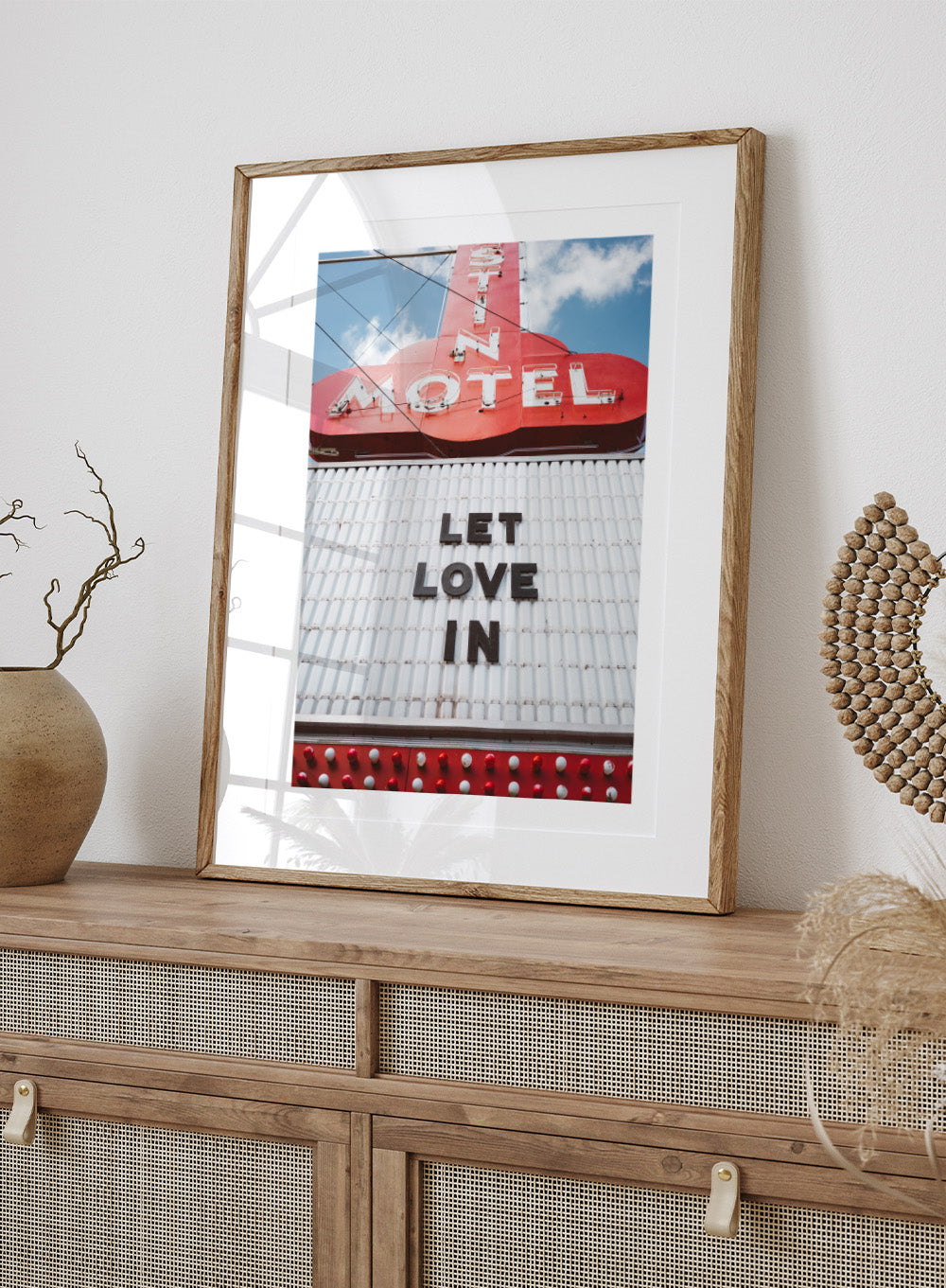 Vintage motel sign with 'Let Love In' message against a blue sky. Let Love In by Bethany Young features a vintage motel sign with red neon lettering against blue sky. Retro Americana photography wall art print.