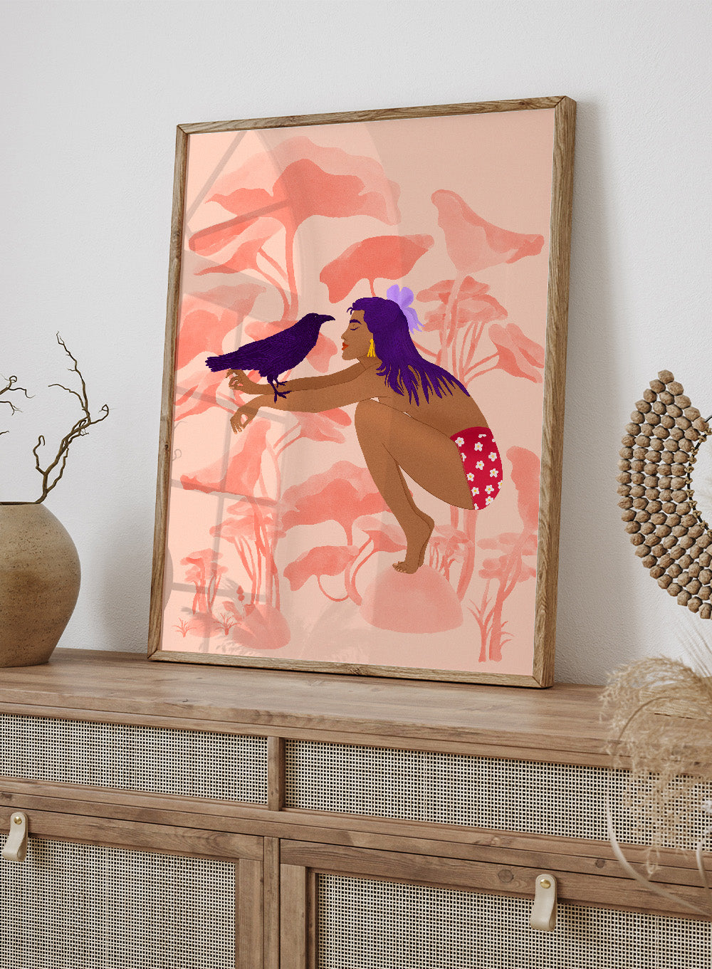 Illustration of a woman with a bird on a pink floral background. Raven by Jota de Jai is a modern pink wall art print of a woman with a purple raven, available as a premium fine art poster with optional wood framing.