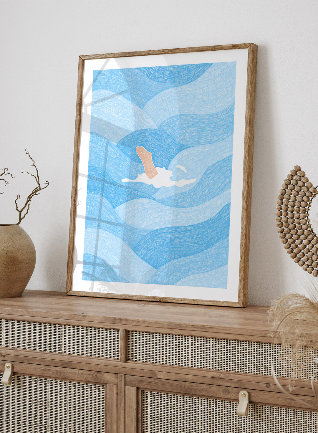 Illustration of a person swimming in blue water with a white border. Hand Reaching Blue Ocean by Rio Soléy is a modern coastal art print featuring swirling blue waves, minimalist illustration, playful design, and contemporary seaside charm.