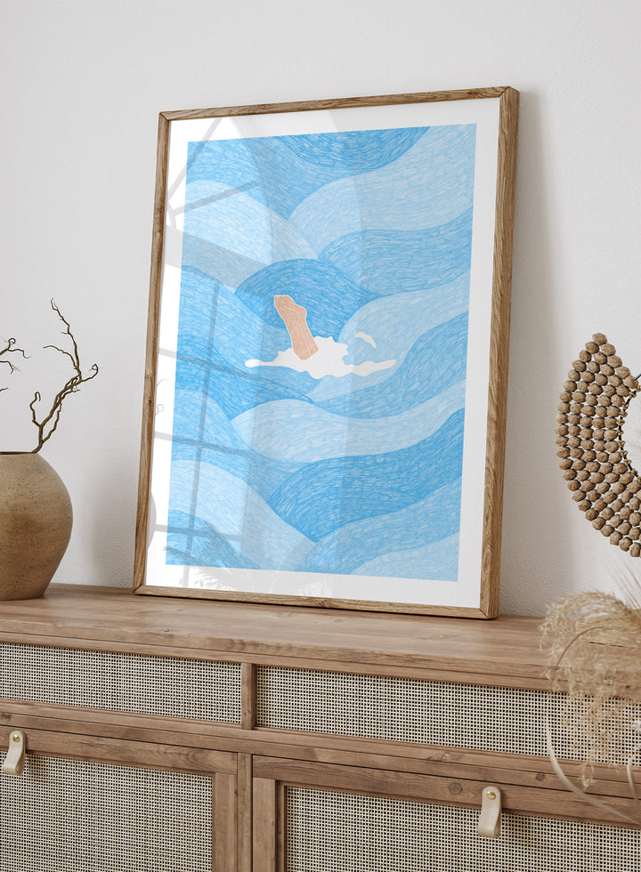 Illustration of a person swimming in blue water with a white border. Hand Reaching Blue Ocean by Rio Soléy is a modern coastal art print featuring swirling blue waves, minimalist illustration, playful design, and contemporary seaside charm.