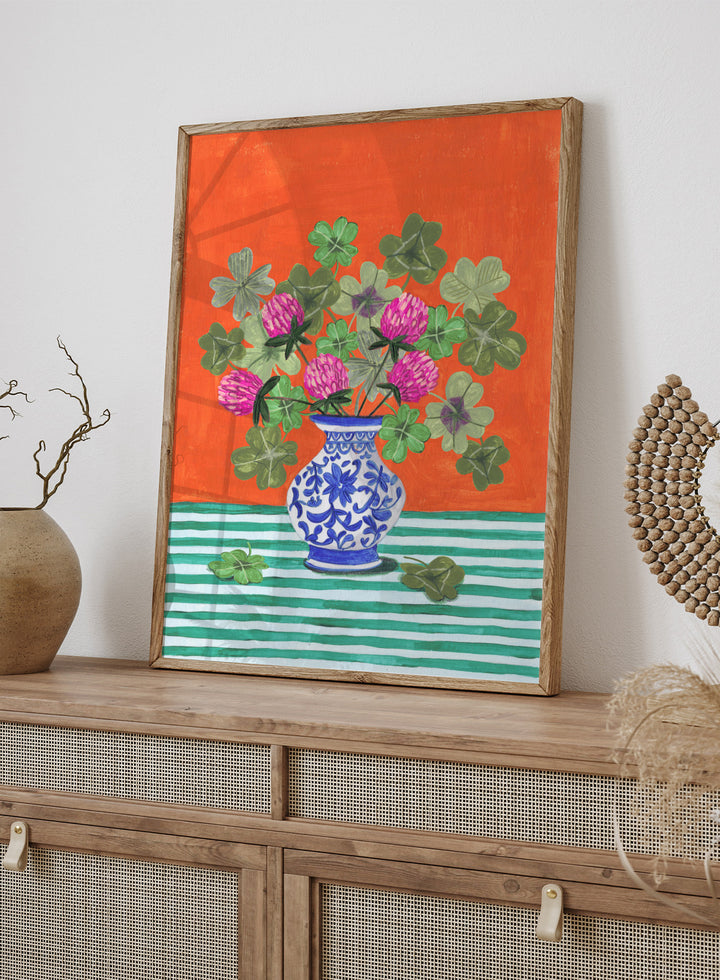 Vase with pink flowers and green leaves on a red and green striped background. Vibrant Clover Still Life by Caroline Bonne Müller is a fine art print and wall poster featuring clover leaves, pink flowers, and a blue vase on a striped table.