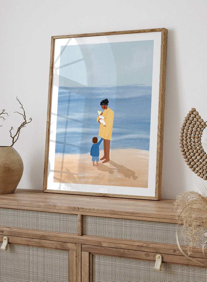 A framed art print featuring an illustration of a man in a yellow striped shirt holding a white dog on a beach next to a child in a blue coat, set against a light blue ocean and pale sky. Family Beach Day by Bea Müller art print featuring a mother with her baby and young child by the sea, created for warm family and coastal decor.
