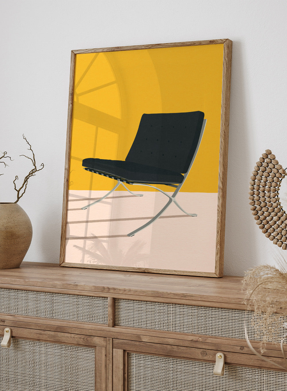 Black chair with metal legs on a yellow and beige background. Barcelona Chair by Mies Van Der Rohe by Rosi Feist is a minimalist modern design art print featuring clean lines and bold color. Officially licensed fine art poster with optional real wood framing, ready to hang.