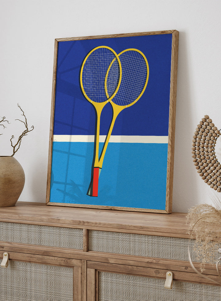 Two yellow badminton rackets on a blue background with a white stripe at the bottom. Wooden Badminton Rackets by Rosi Feist is a modern minimalist fine art print featuring bold yellow rackets on a graphic blue court. Officially licensed wall poster with optional artisan framing.