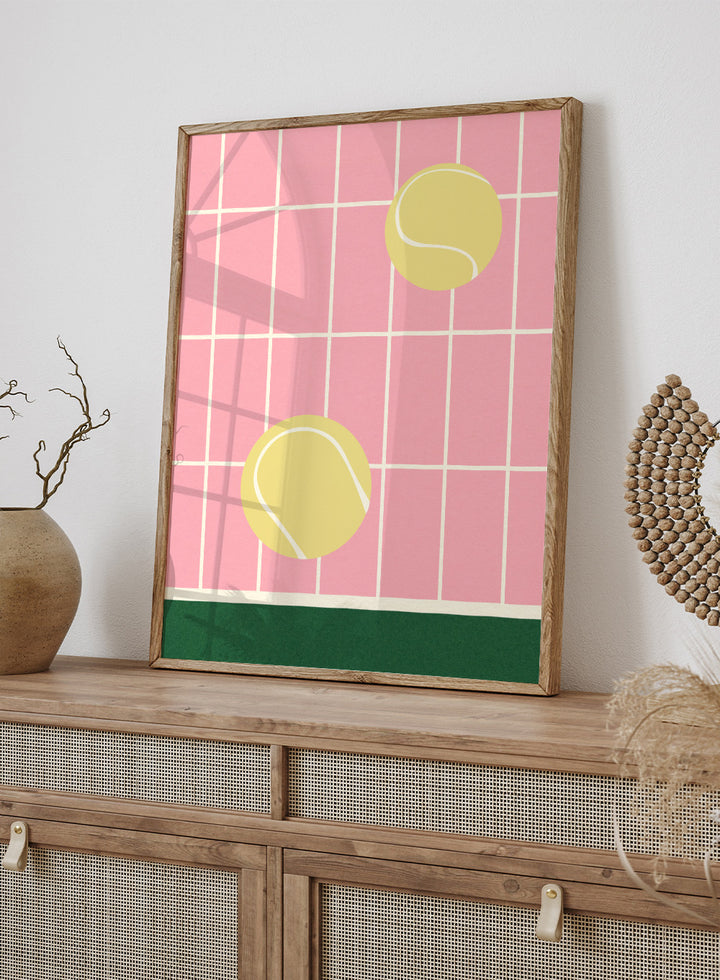 Two yellow tennis balls on a pink grid background with a green stripe at the bottom. Tennis Kitchen by Rosi Feist is a modern minimalist fine art print featuring oversized tennis balls on pink tile. Officially licensed wall poster with optional artisan framing.