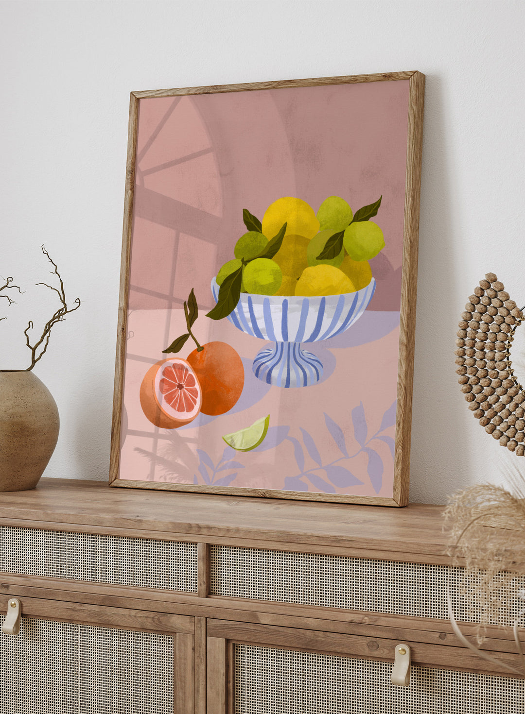 Illustration of a bowl with lemons and limes on a pink background. Bittersweet by Goed Blauw is a still life art print and wall poster with lemons, limes, and grapefruit in a striped bowl on a soft pink background.