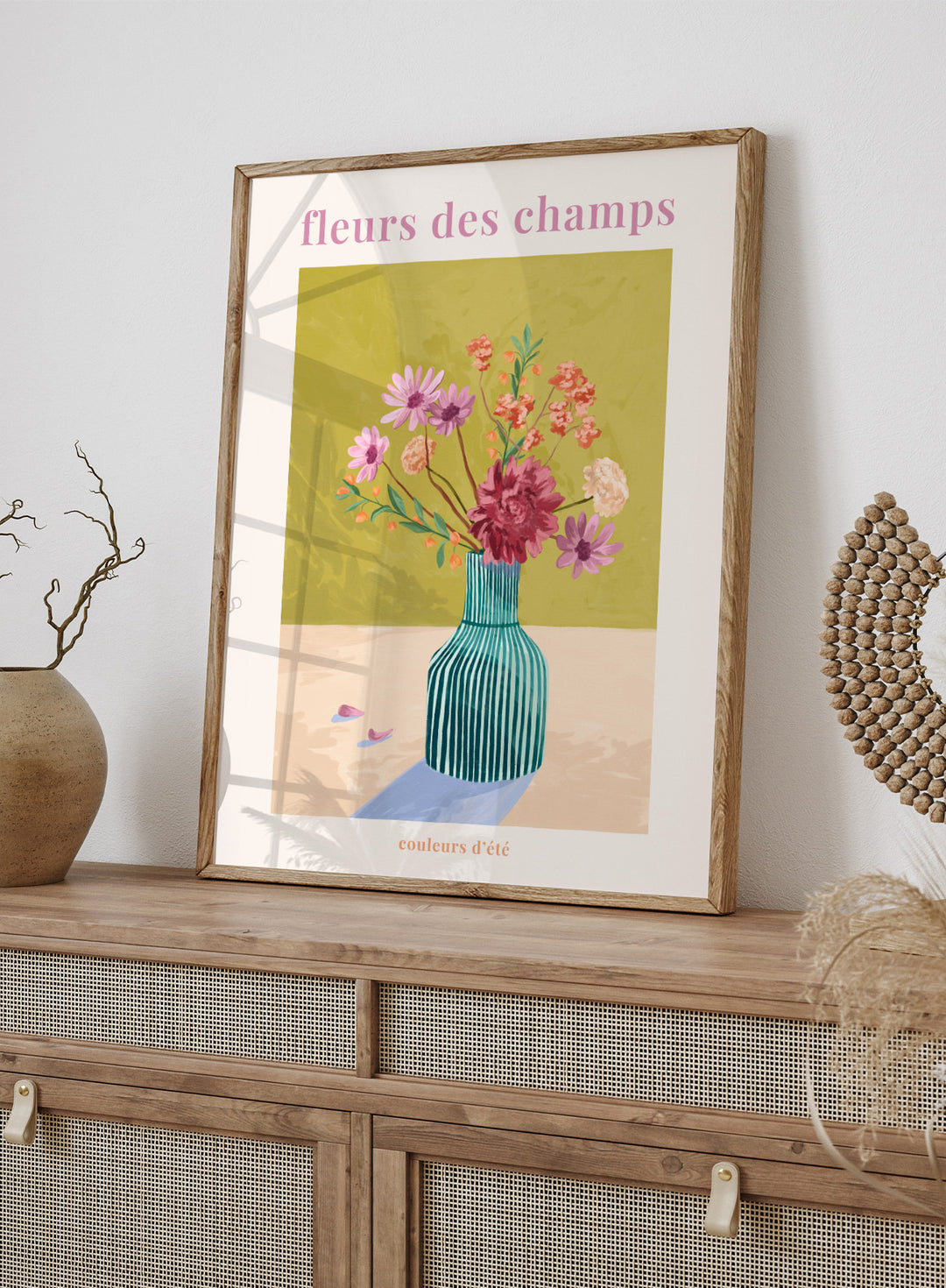 Illustration of a vase with flowers on a green background, featuring the text 'fleurs des champs' and 'couleurs d'ete'. Fleur Des Champs Green by Goed Blauw is a colorful floral art print and wall poster featuring a striped vase with loose flowers on a warm yellow background.