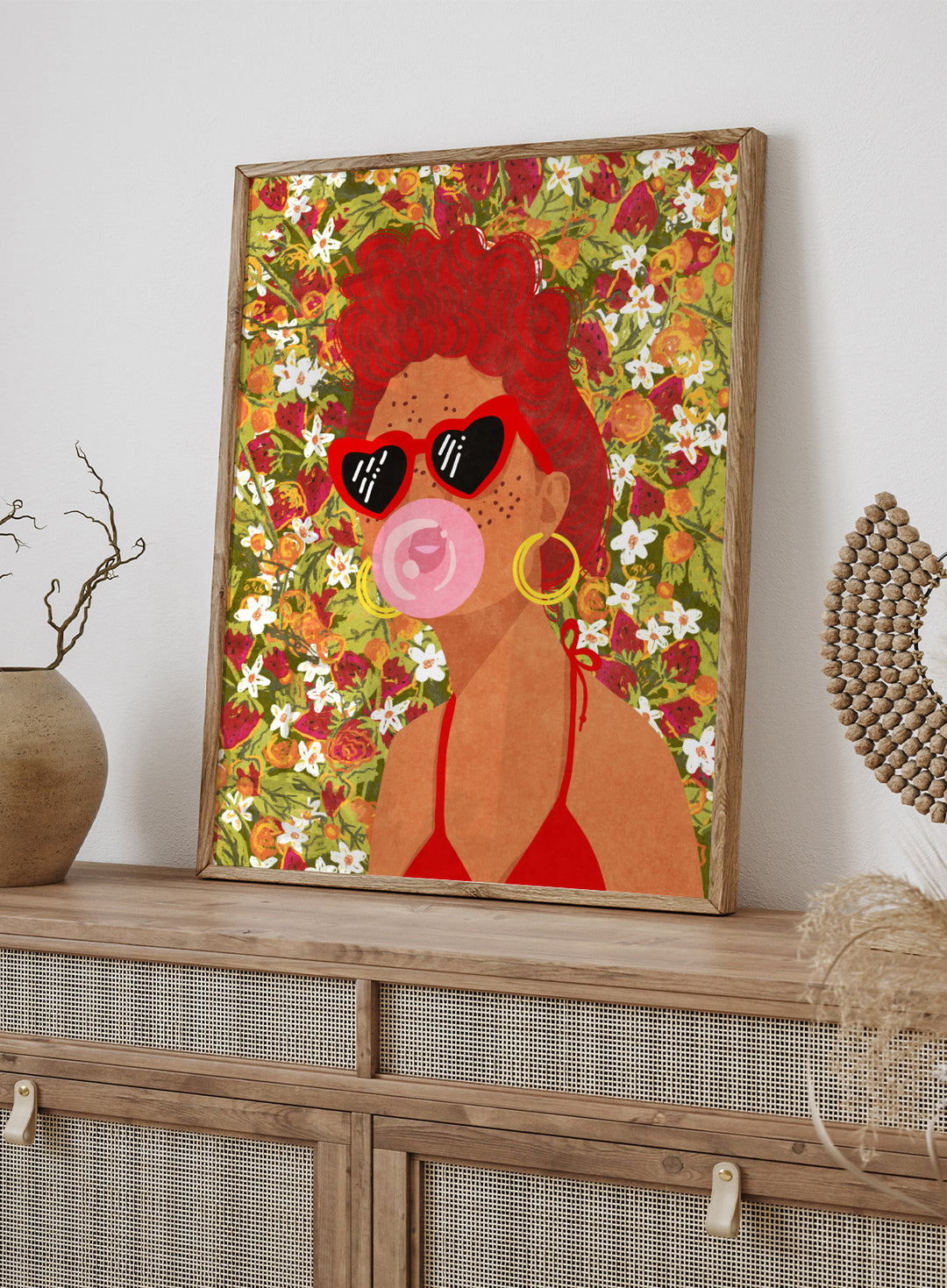 Illustration of a woman with red hair, sunglasses, and a pink bubble gum against a floral background. Strawberry Lady by Raissa Oltmanns fine art print featuring bold female portrait with strawberry background, modern colorful wall decor poster.