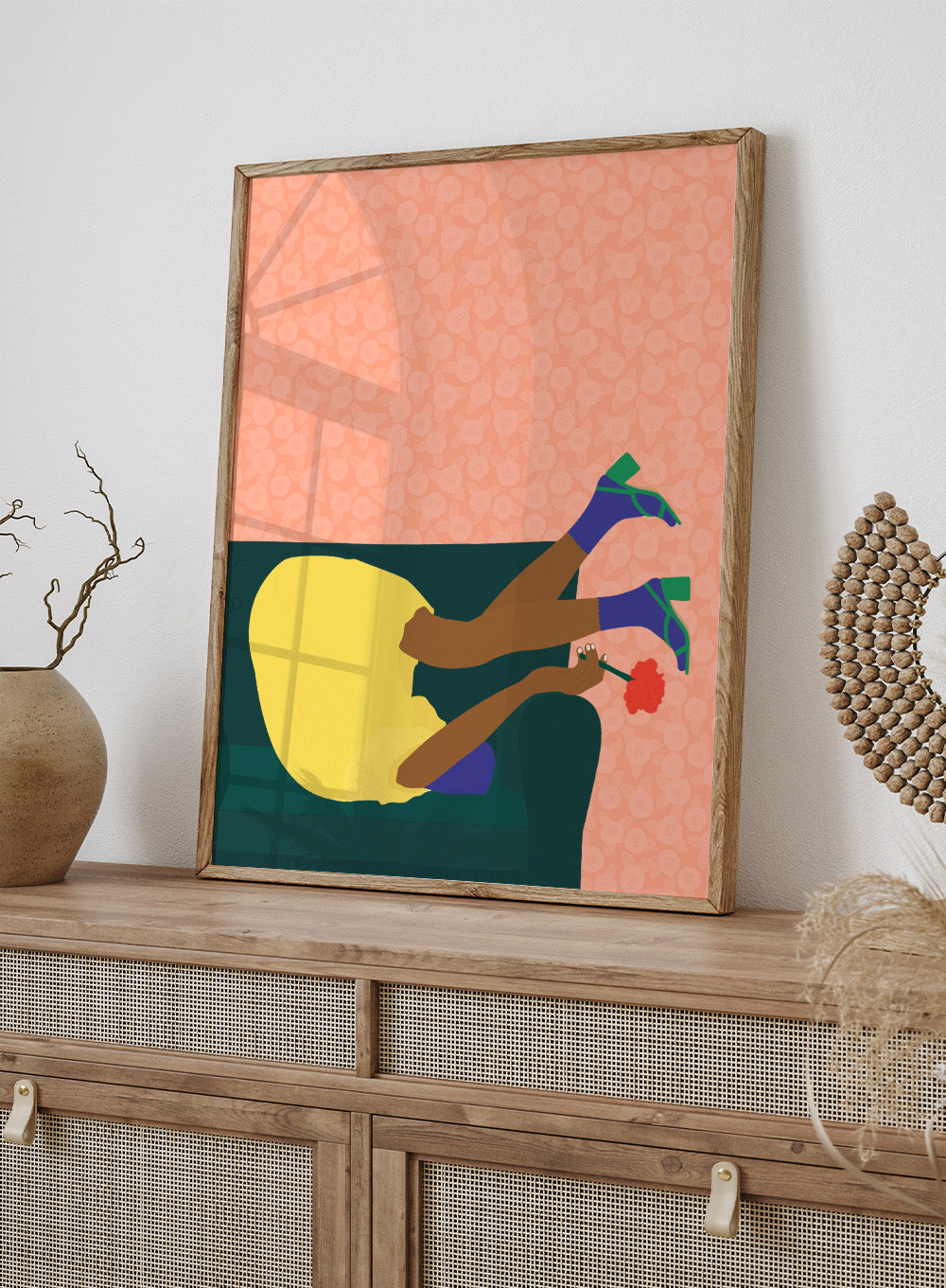 Illustration of a person sitting on a couch with a flower, against a patterned pink background. New Year’s Eve by Jota De Jai is a playful modern fine art print of a woman upside down on a couch in heels and a yellow dress. Available framed or unframed.