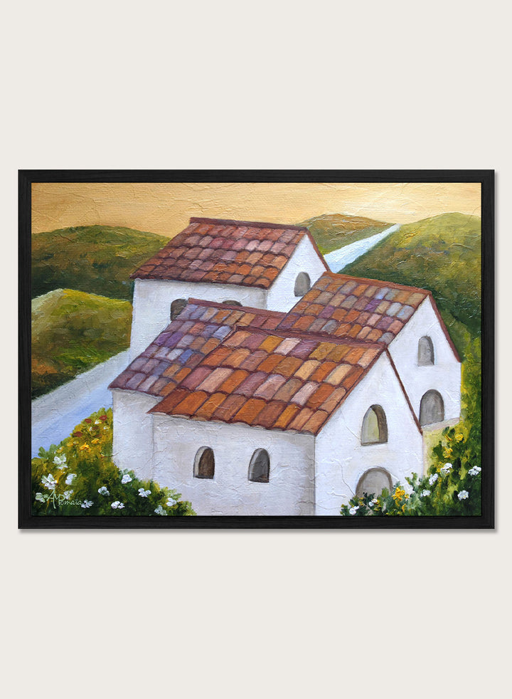 A framed landscape painting depicting two white buildings with terracotta tiled roofs nestled in green hills, with a winding light blue road and a warm yellow sky. Shop Tuscan Hillside Village by Angeles M. Pomata, a warm countryside landscape art print featuring white houses, terracotta roofs, green hills, and wildflowers.