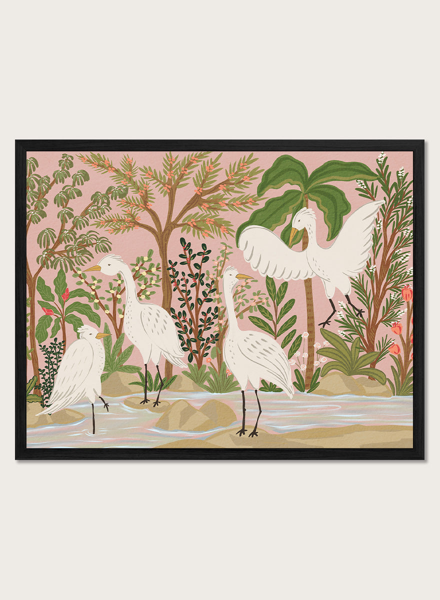 A framed art print featuring a stylized illustration of four white cranes in a tropical landscape with palm trees, green foliage, and a pink sky, displayed on a light beige wall. Shop Peaceful Jungle Egrets by Nikita Jariwala, a tropical bird wall art print featuring white egrets, lush greenery, botanical detail, and soft pink tones.a
